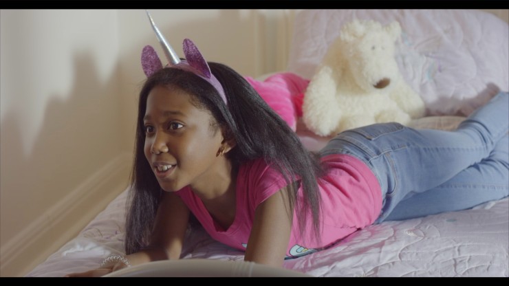 A young Black girl laying down smiling and wearing a unicorn headband