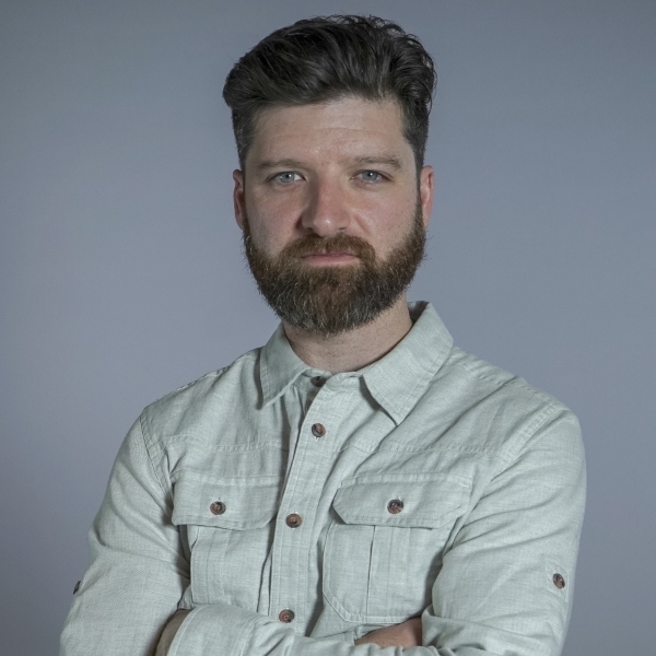 Headshot of a man with short brown hair and a beard in a button up cream shirt with his arms crossed