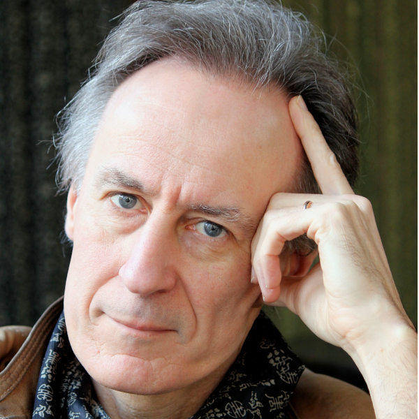 An man with grey hair leans his head on his hand and looks at camera.