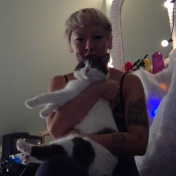 photo of artist Sarah Boo, holding a cat who is white with tabby markings 