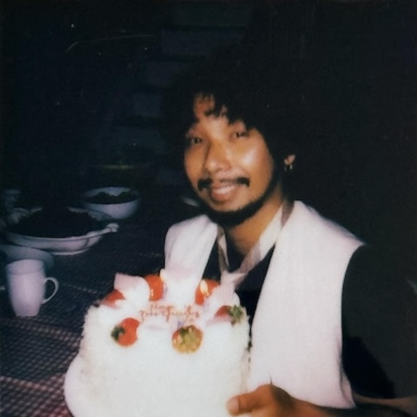 Man in a tie and suit vest holds a birthday cake, looking at camera.