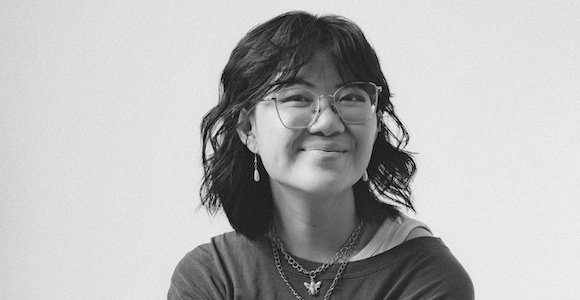 Black and white photo of a seated woman with short dark hair and wearing glasses.