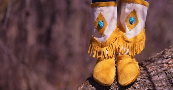 Closeup of the feet and lower legs of a person wearing moccasins that are yellow and white with a turquoise stone.