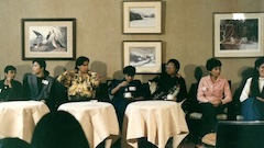 A group of women of colour engaged in conversation while seated at tables in a well-lit room.