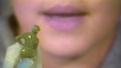 A child with pink lips holds a green soldier toy in front of their mouth