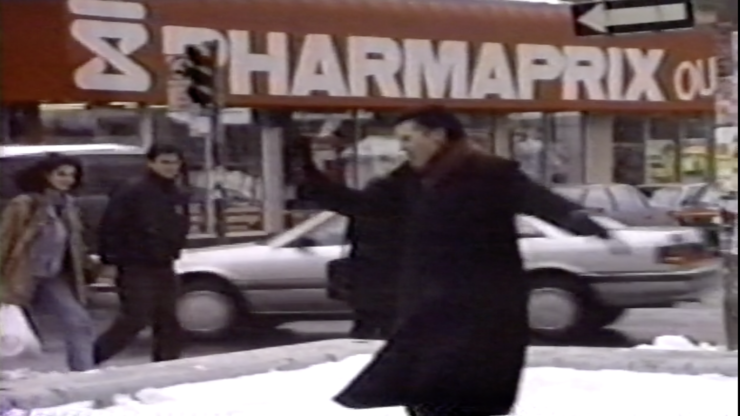 A woman with short hair in a black coat twirls on a snowy sidewalk near a Pharmaprix store, with a m