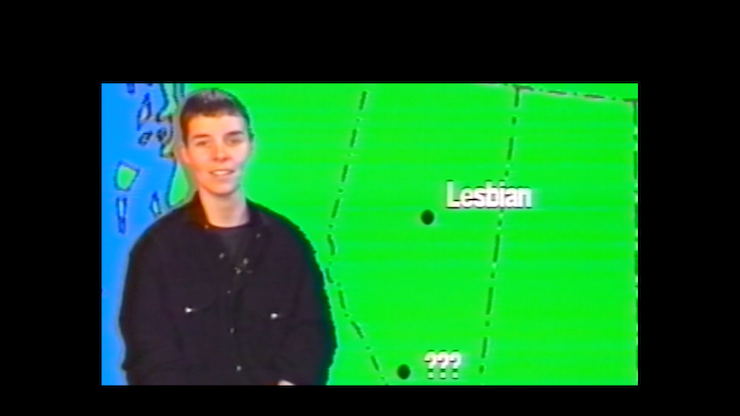 A person stands in front of a screen reminiscent of a weatherperson.