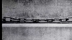 A black and white film still of a chain