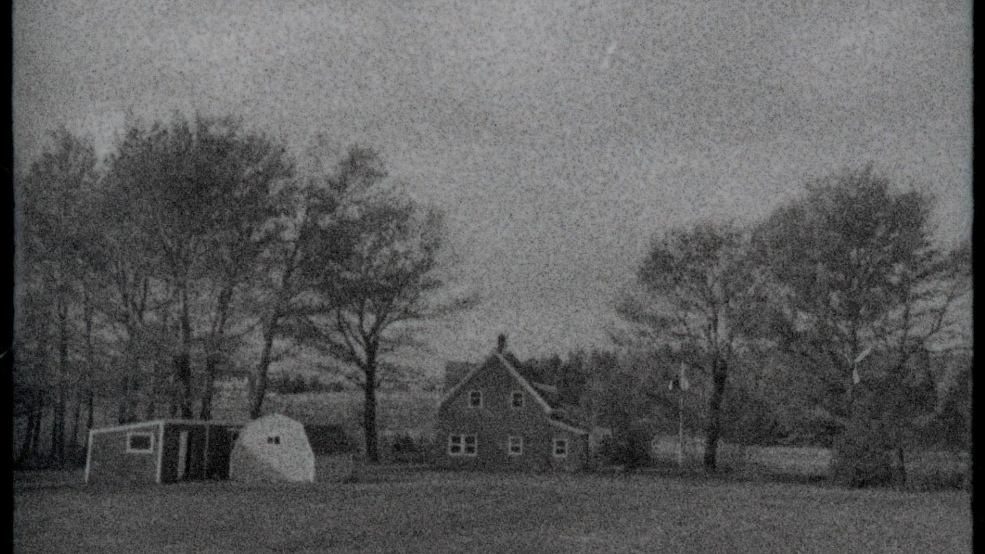 A black and white photo of a house and trees in the distance