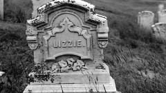 Black and white still image of an ornamental tombstone with the name "Lizzie" carved in the front.