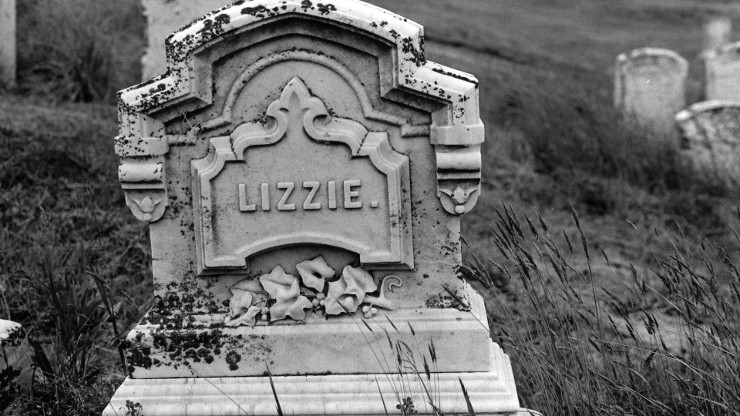 Black and white still image of an ornamental tombstone with the name "Lizzie" carved in the front.