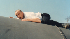 A man in business casual lies on his stomach on a curved structure.