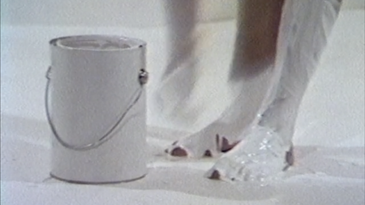 Colour image of a white paint can and a person bent over with white paint covering their feet/.