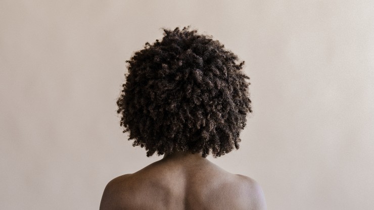 A Black woman facing a beige wall with a Black hair afro