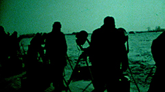 A group of people with telescopes are seen on a green snowy landscape. There bodies are silhouetted.