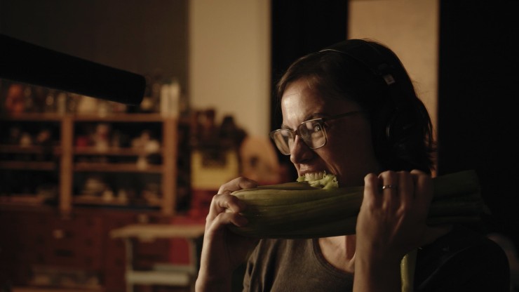 A woman with short hair and glasses biting into celery