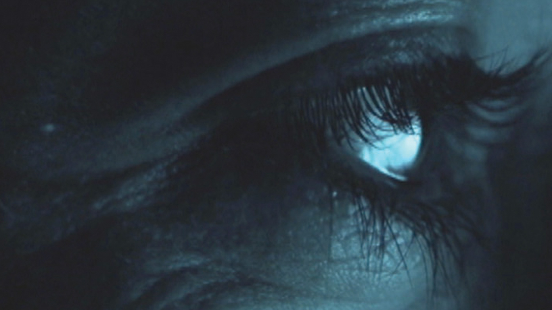 Close up of a woman's eye, seen from the side of her face. The colour image is taken in a dark environment and has dark blue tones.