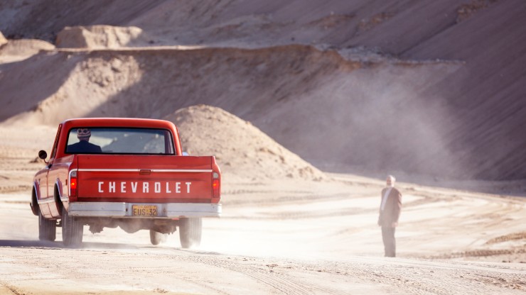 A red pick up truck driving away from a man in the dessert