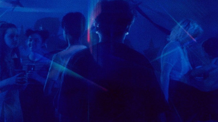A boy walks through a crowd of people dancing, the lighting is blue 