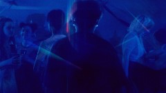 A boy walks through a crowd of people dancing, the lighting is blue 