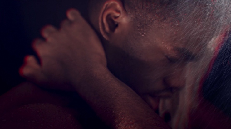 A Black man with his eyes closed in a shower, his hand is holding the back of his neck