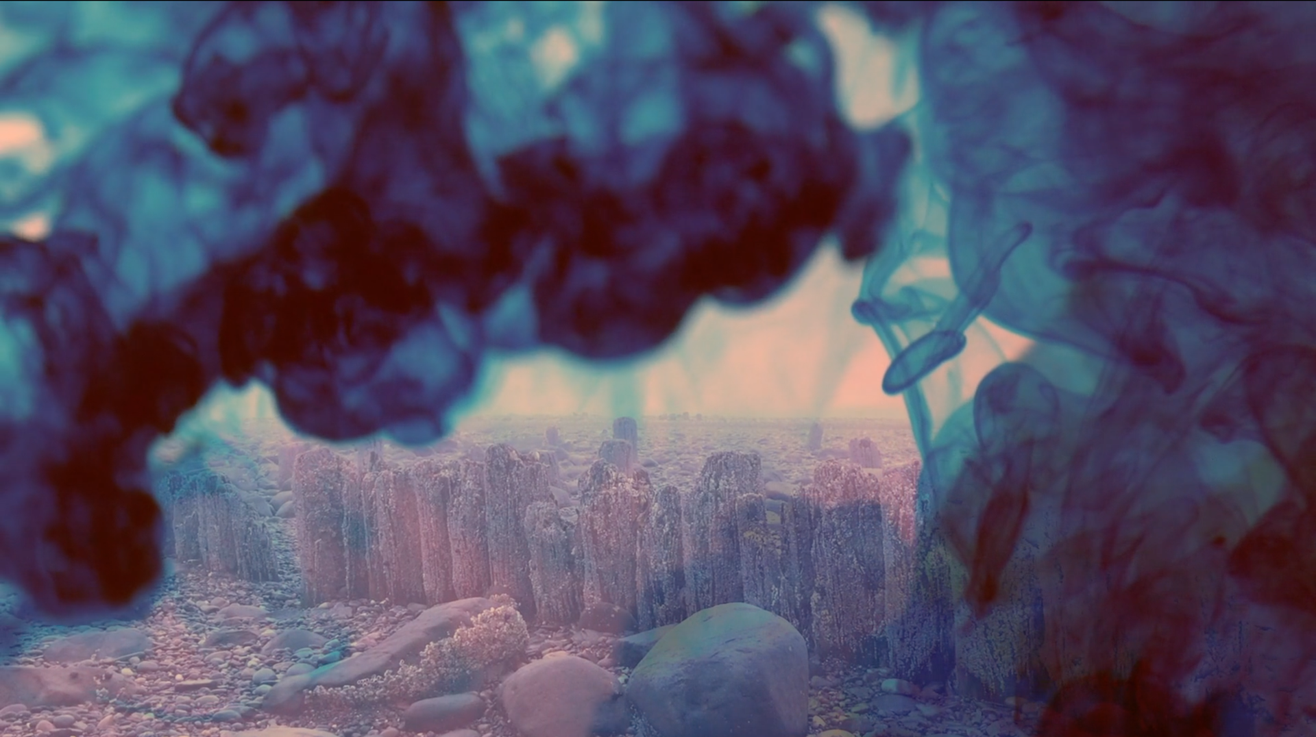 Un arrêt sur image de l'encre bleue dans l'eau avec des rochers et des cailloux derrière.